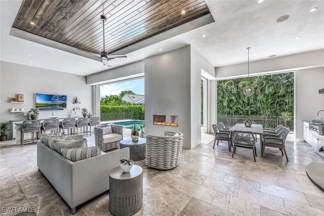 living room featuring a tray ceiling, ceiling fan, a fireplace, and wood ceiling