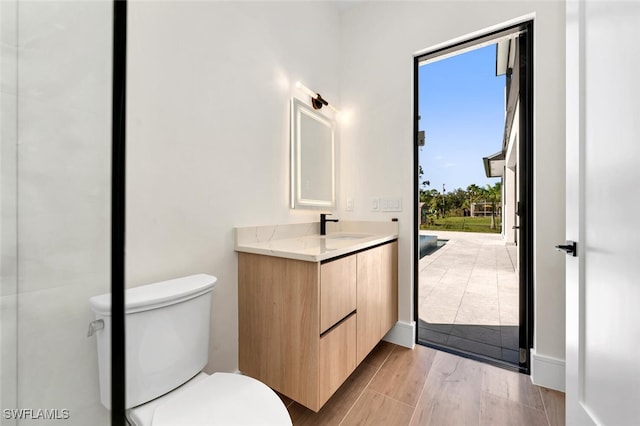 bathroom with toilet, baseboards, wood finished floors, and vanity