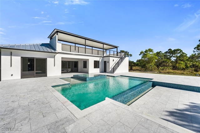 rear view of house featuring metal roof, a standing seam roof, stairs, a patio area, and stucco siding