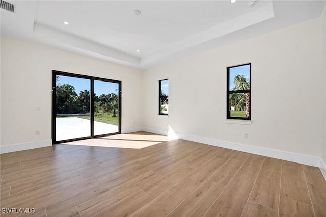 spare room with light wood finished floors, visible vents, a tray ceiling, and baseboards