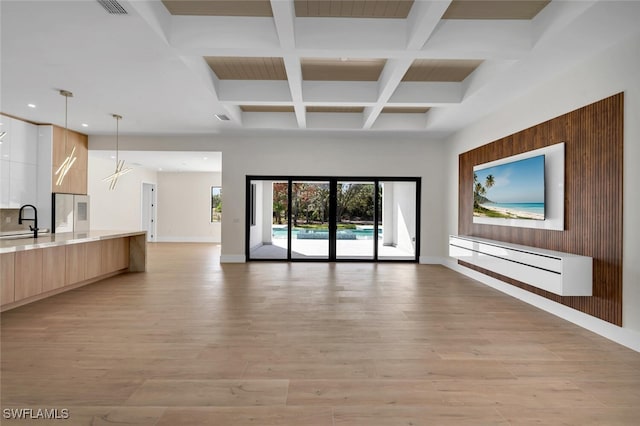 unfurnished living room with light wood-style floors, a baseboard radiator, beam ceiling, and a sink