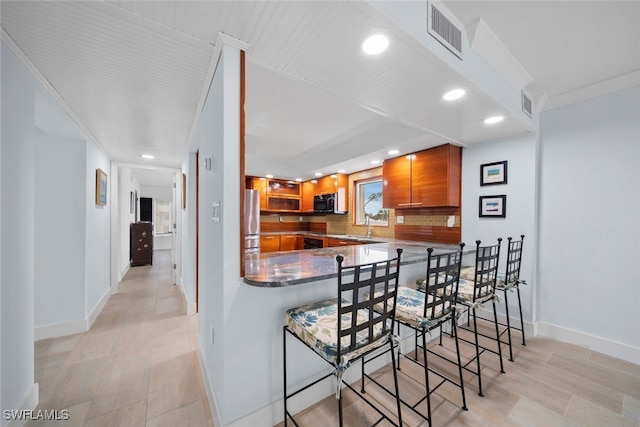 kitchen featuring crown molding, stainless steel fridge, backsplash, a kitchen breakfast bar, and kitchen peninsula