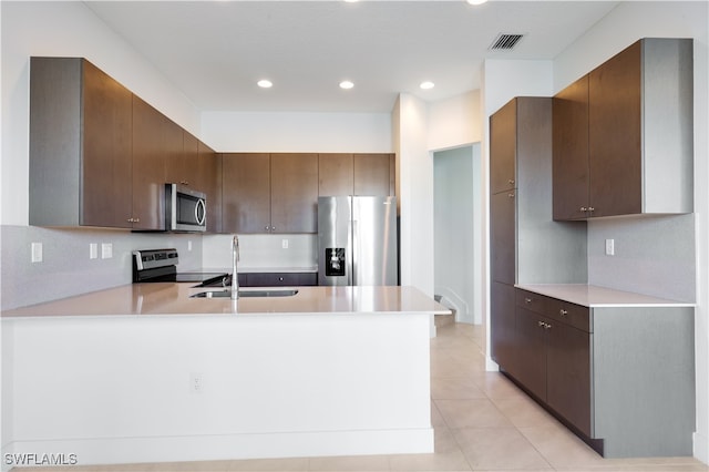 kitchen with sink, kitchen peninsula, dark brown cabinets, light tile patterned flooring, and appliances with stainless steel finishes