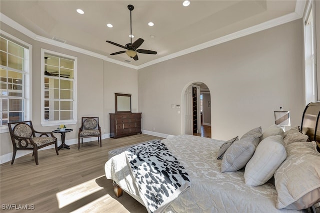 bedroom featuring baseboards, arched walkways, light wood-style floors, and crown molding