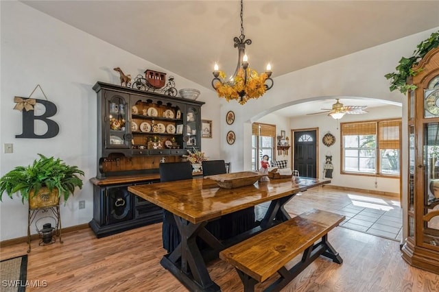 dining space with lofted ceiling, ceiling fan with notable chandelier, and light wood-type flooring