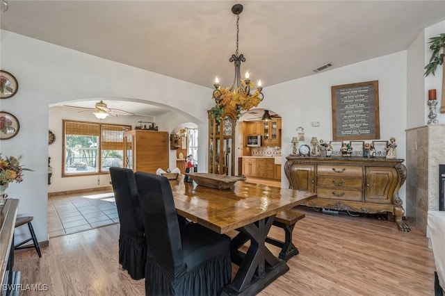 dining room with lofted ceiling, ceiling fan with notable chandelier, a fireplace, and light hardwood / wood-style floors