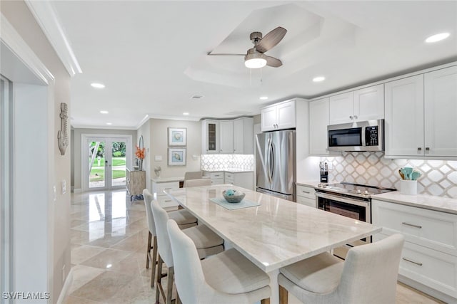 kitchen featuring light stone countertops, a kitchen breakfast bar, backsplash, white cabinets, and appliances with stainless steel finishes