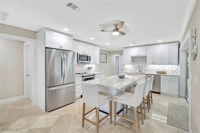 kitchen with stainless steel appliances, a kitchen breakfast bar, tasteful backsplash, light stone counters, and white cabinets