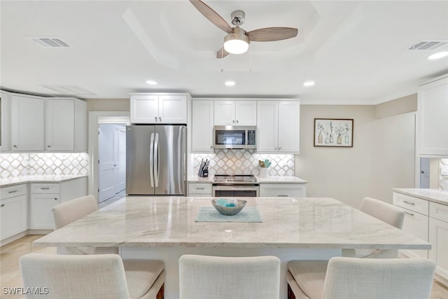 kitchen featuring decorative backsplash, appliances with stainless steel finishes, a kitchen breakfast bar, light stone counters, and light hardwood / wood-style floors