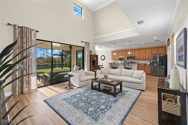 living room with a high ceiling, crown molding, a wealth of natural light, and light hardwood / wood-style flooring