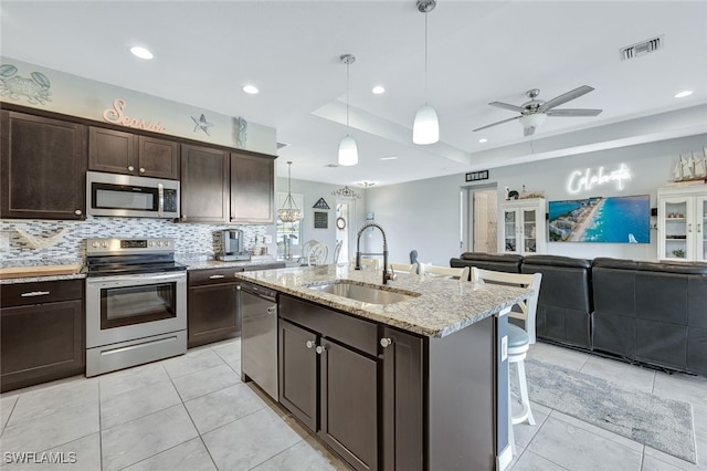 kitchen with sink, decorative light fixtures, appliances with stainless steel finishes, a raised ceiling, and an island with sink