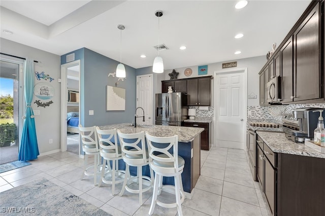 kitchen with sink, hanging light fixtures, an island with sink, stainless steel appliances, and backsplash