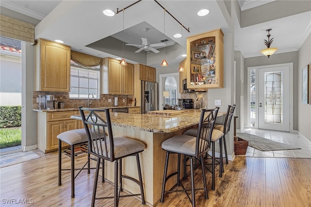 kitchen with crown molding, stainless steel appliances, decorative light fixtures, and light hardwood / wood-style floors