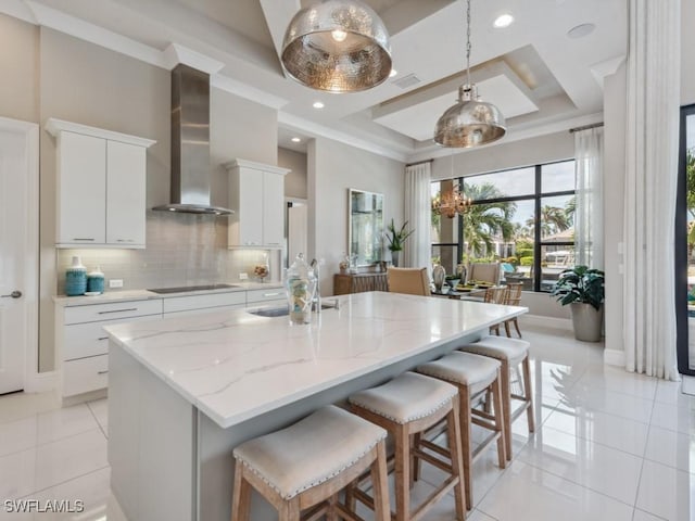 kitchen with wall chimney range hood, decorative light fixtures, black electric cooktop, a center island with sink, and white cabinets