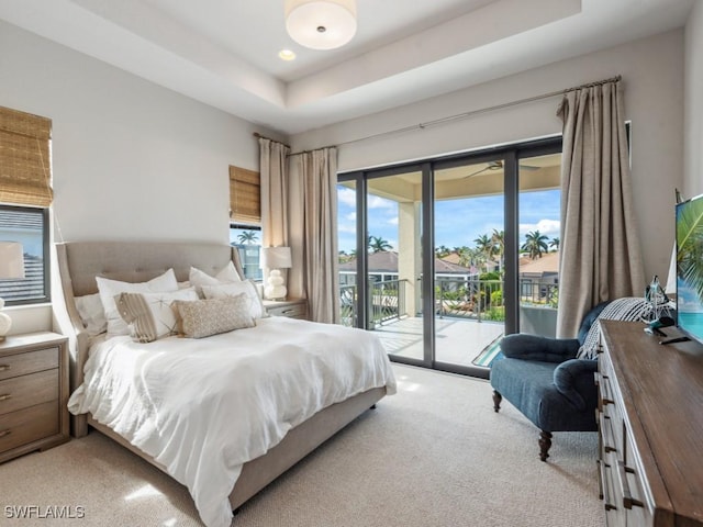 carpeted bedroom with a tray ceiling, access to exterior, and multiple windows