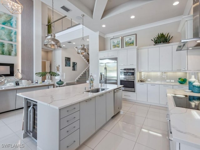 kitchen with wall chimney range hood, white cabinetry, hanging light fixtures, and sink