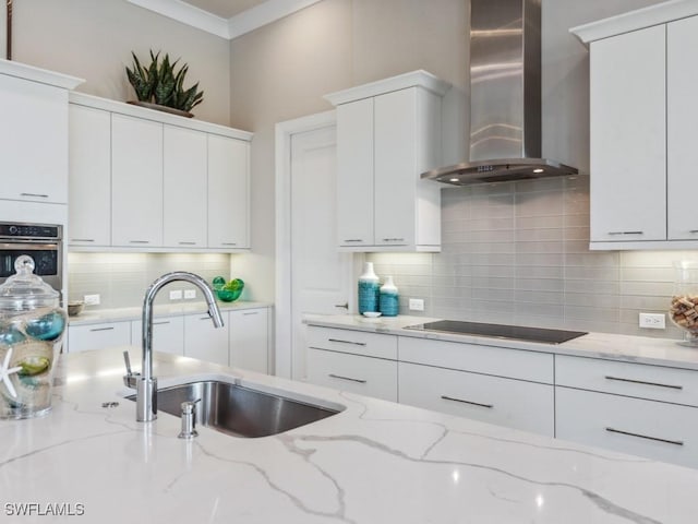 kitchen with oven, white cabinetry, light stone countertops, and wall chimney range hood