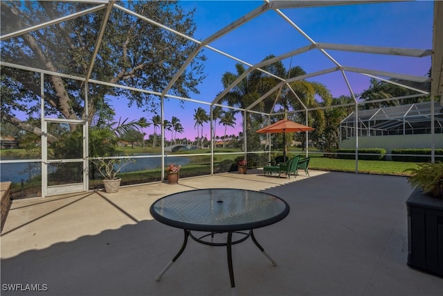 patio terrace at dusk with a water view, a yard, and glass enclosure