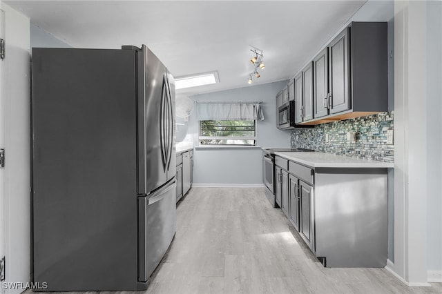 kitchen featuring gray cabinetry, vaulted ceiling, decorative backsplash, light wood-type flooring, and appliances with stainless steel finishes