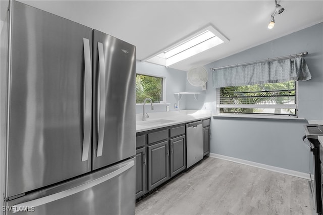 kitchen with sink, vaulted ceiling with skylight, gray cabinets, appliances with stainless steel finishes, and light hardwood / wood-style floors