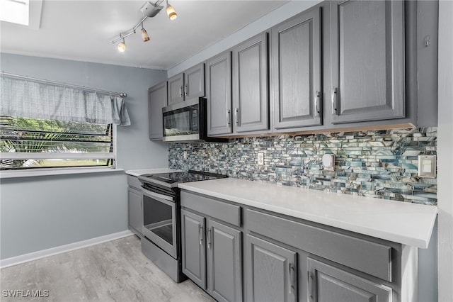 kitchen featuring gray cabinetry, stainless steel appliances, tasteful backsplash, crown molding, and light hardwood / wood-style floors