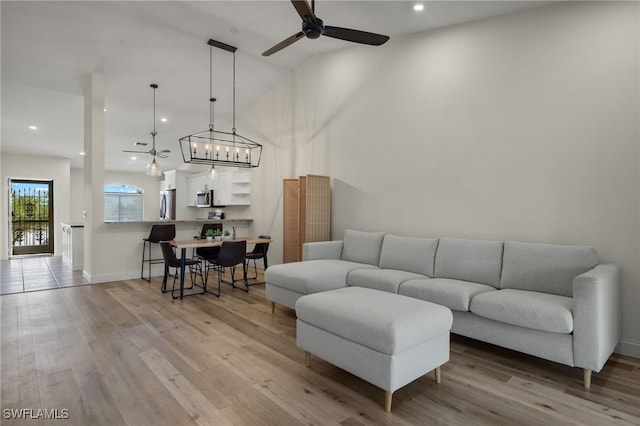 living room featuring ceiling fan, a towering ceiling, and light hardwood / wood-style floors