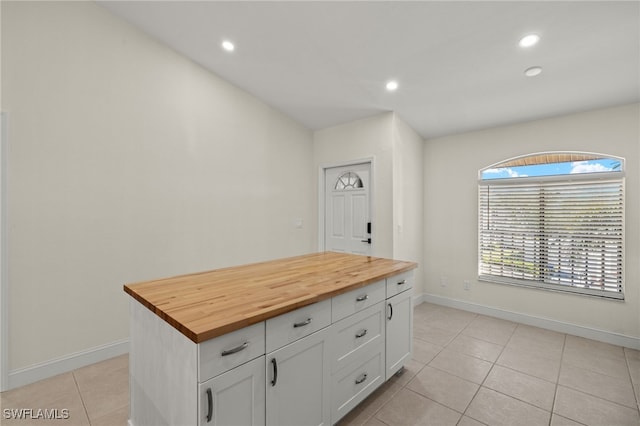 kitchen with a center island, light tile patterned floors, white cabinets, and wood counters