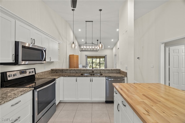 kitchen featuring butcher block countertops, sink, appliances with stainless steel finishes, hanging light fixtures, and white cabinets