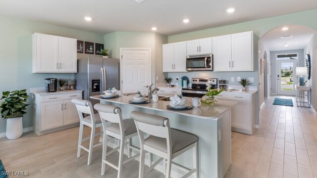 kitchen with white cabinetry, stainless steel appliances, a kitchen breakfast bar, and a center island with sink