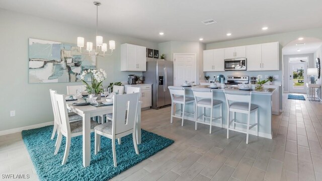 kitchen with appliances with stainless steel finishes, a kitchen island with sink, white cabinets, and decorative light fixtures