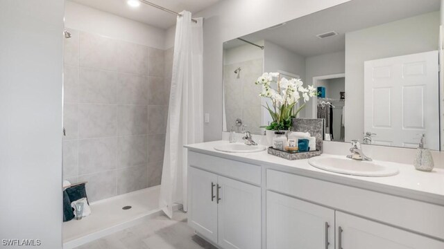 bathroom with double vanity, visible vents, a sink, and tiled shower