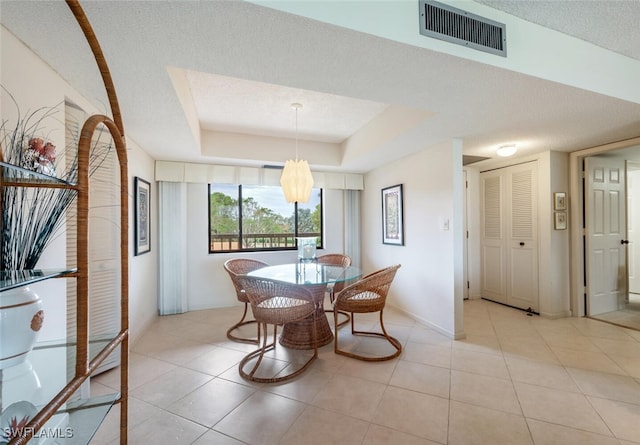 tiled dining area with a notable chandelier, a raised ceiling, and a textured ceiling