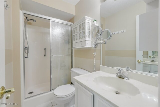 bathroom with tile patterned flooring, vanity, toilet, and a shower with door