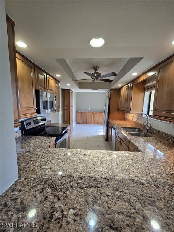 kitchen with appliances with stainless steel finishes, sink, dark stone countertops, a tray ceiling, and crown molding