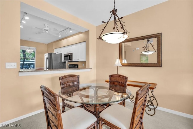 carpeted dining area with rail lighting, a ceiling fan, and baseboards