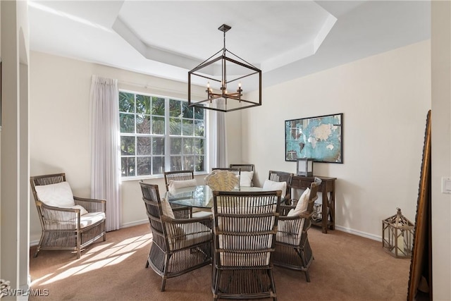 carpeted dining area featuring a chandelier and a tray ceiling