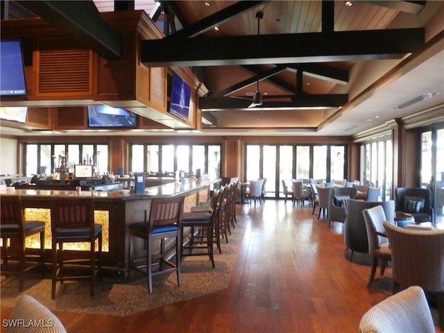 bar with lofted ceiling with beams, a wealth of natural light, ceiling fan, and wood-type flooring