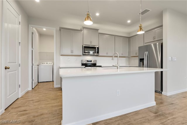 kitchen with washer / clothes dryer, appliances with stainless steel finishes, sink, and a center island with sink