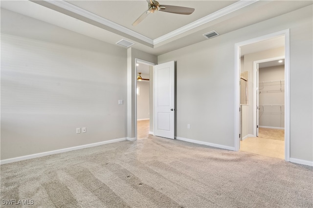 unfurnished bedroom featuring light carpet, ceiling fan, a walk in closet, and a raised ceiling