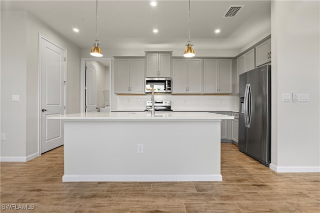 kitchen featuring gray cabinets, an island with sink, appliances with stainless steel finishes, decorative backsplash, and pendant lighting