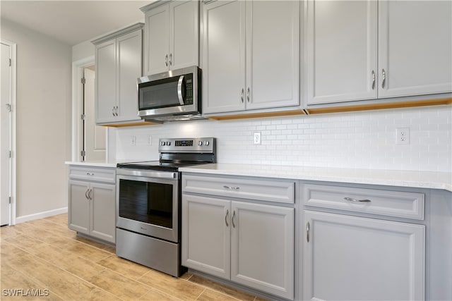 kitchen featuring decorative backsplash, appliances with stainless steel finishes, gray cabinetry, and light stone counters