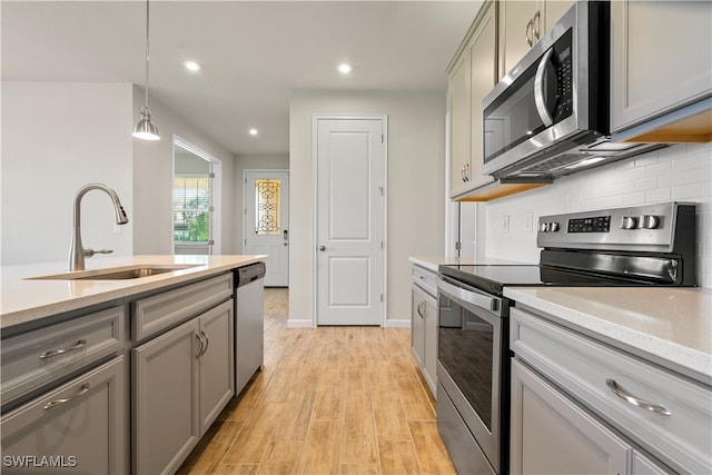 kitchen with gray cabinets, pendant lighting, sink, light wood-type flooring, and stainless steel appliances