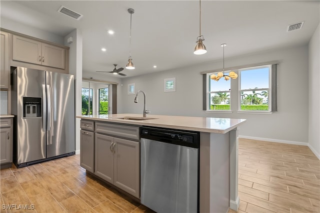 kitchen featuring gray cabinets, an island with sink, appliances with stainless steel finishes, hanging light fixtures, and sink