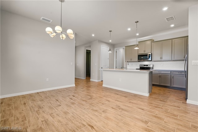 kitchen with decorative light fixtures, appliances with stainless steel finishes, gray cabinets, and a center island with sink