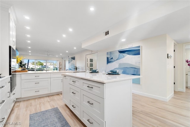 kitchen with kitchen peninsula, ceiling fan, a center island, light hardwood / wood-style floors, and white cabinetry