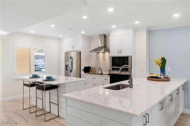 kitchen featuring wall chimney exhaust hood, white cabinetry, a large island with sink, and appliances with stainless steel finishes