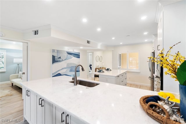 kitchen with a kitchen island with sink, sink, white cabinets, and light hardwood / wood-style floors