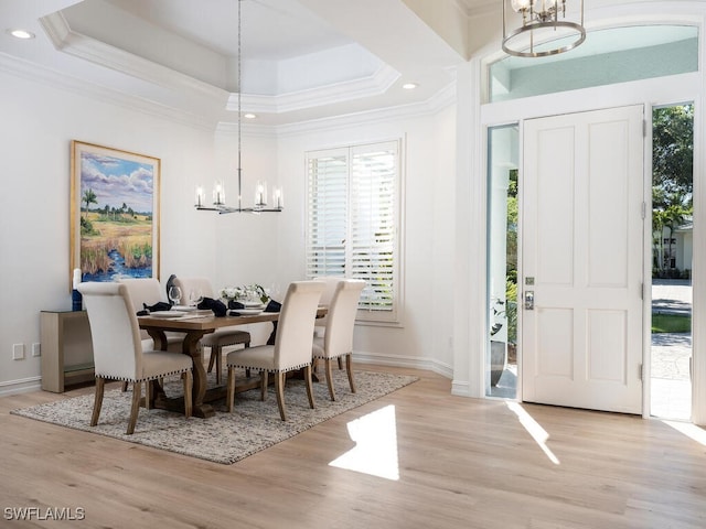 dining area featuring a chandelier, light hardwood / wood-style floors, a raised ceiling, and ornamental molding