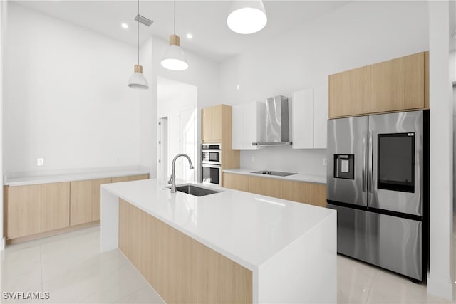 kitchen featuring pendant lighting, a center island with sink, wall chimney exhaust hood, white cabinetry, and stainless steel appliances