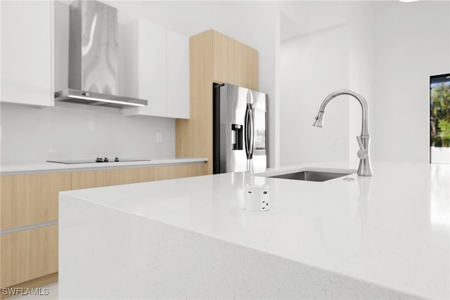 kitchen featuring sink, wall chimney range hood, stainless steel fridge with ice dispenser, black electric cooktop, and white cabinets